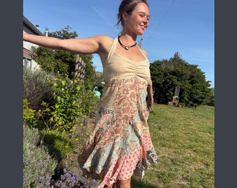 May include: A halter-neck dress with a beige bodice and a patchwork skirt featuring floral and geometric patterns in pink, blue, and beige. The dress is worn outdoors on a sunny day.