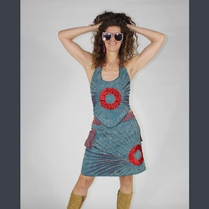 May include: A blue halter dress with red and white geometric designs. The dress has a fitted bodice and a flared skirt. The model is wearing sunglasses.