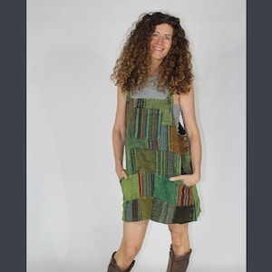 May include: A green patchwork overall dress with a variety of patterns and textures. The dress has two large pockets on the front and a simple design.