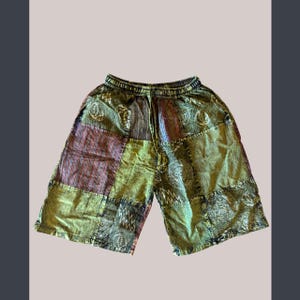 Peut inclure: Shorts patchwork aux tons de vert, marron et bordeaux. Le short a une taille élastique et divers carrés de tissu à motifs. Le short, qui arrive au genou, semble être fait d'une matière légère.