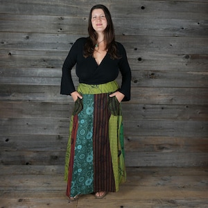 Puede incluir: Una falda larga de retazos multicolores con un estampado floral verde, marrón y azul. La falda tiene una cintura ancha y bolsillos a los lados.