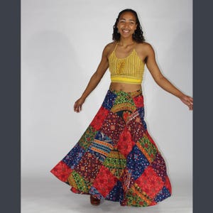 Puede incluir: Una mujer con un top halter amarillo y una falda larga de patchwork de colores. La falda tiene una variedad de patrones y colores, incluyendo rojo, azul, verde y amarillo.