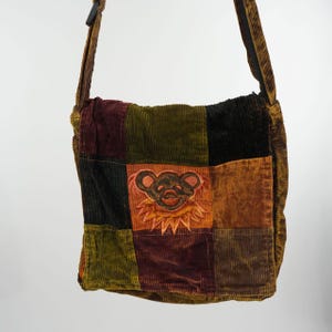 Könnte beinhalten: Eine Cord-Umhängetasche mit Patchwork-Design in Braun-, Grün- und Schwarztönen. Die Tasche hat ein gesticktes Bärenmuster auf der Vorderseite. Der Riemen ist braun und verstellbar.
