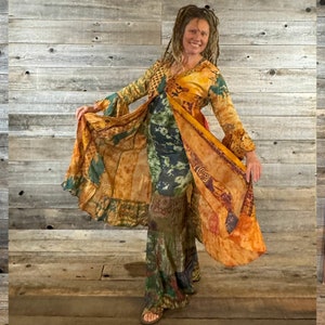 May include: A woman wearing a long, flowing, multi-colored dress with a patchwork design. The dress has a long, flowing skirt and a fitted bodice. The woman is standing in front of a wooden wall.