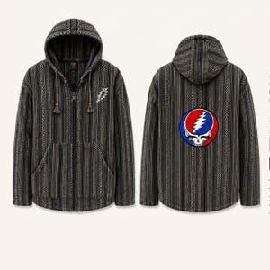 Puede incluir: Una sudadera con cremallera y capucha con un patrón de rayas verticales en negro y gris. La parte delantera muestra un pequeño logotipo de rayo blanco, mientras que la parte trasera presenta un gran gráfico circular de una calavera.