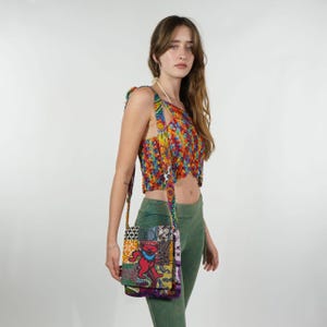 Könnte beinhalten: Eine bunte Patchwork-Umhängetasche mit einem lebendigen Bären-Motiv. Die Tasche hat einen langen Riemen und eine rechteckige Form. Die Oberseite und der Riemen der Tasche bestehen aus einem Patchwork aus verschiedenen Stoffen. Die Person trägt ein passendes Patchwork-Top und grüne Hosen.