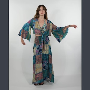 Peut inclure: Un ensemble patchwork comprenant un haut noué à manches évasées, un haut dos nu assorti et une longue jupe. L'ensemble présente des motifs cachemire turquoise, rose et or. La jupe a une taille élastique. La tenue est conçue pour une esthétique bohème.