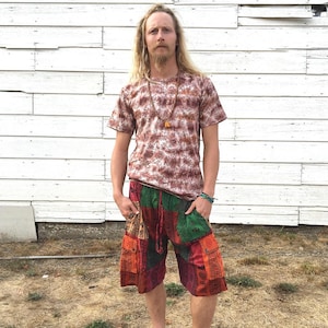 Puede incluir: Una persona que lleva una camisa de manga corta con estampado marrón y blanco con un collar de cuentas y pantalones cortos de patchwork de colores.