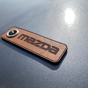 May include: A brown leather keychain with a silver ring and the word "MAZDA" engraved in black lettering.