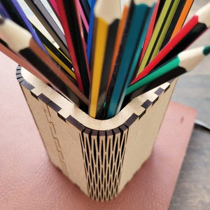 May include: A wooden pencil holder with a unique, intricate design. The holder is filled with a variety of coloured pencils, including red, blue, green, yellow, and black.