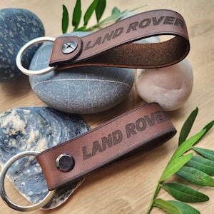 May include: Two brown leather keychains with silver key rings. Both keychains have the words "LAND ROVER" embossed in the leather.