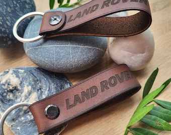 May include: Two brown leather keychains with silver key rings. Both keychains have the words "LAND ROVER" embossed in the leather.