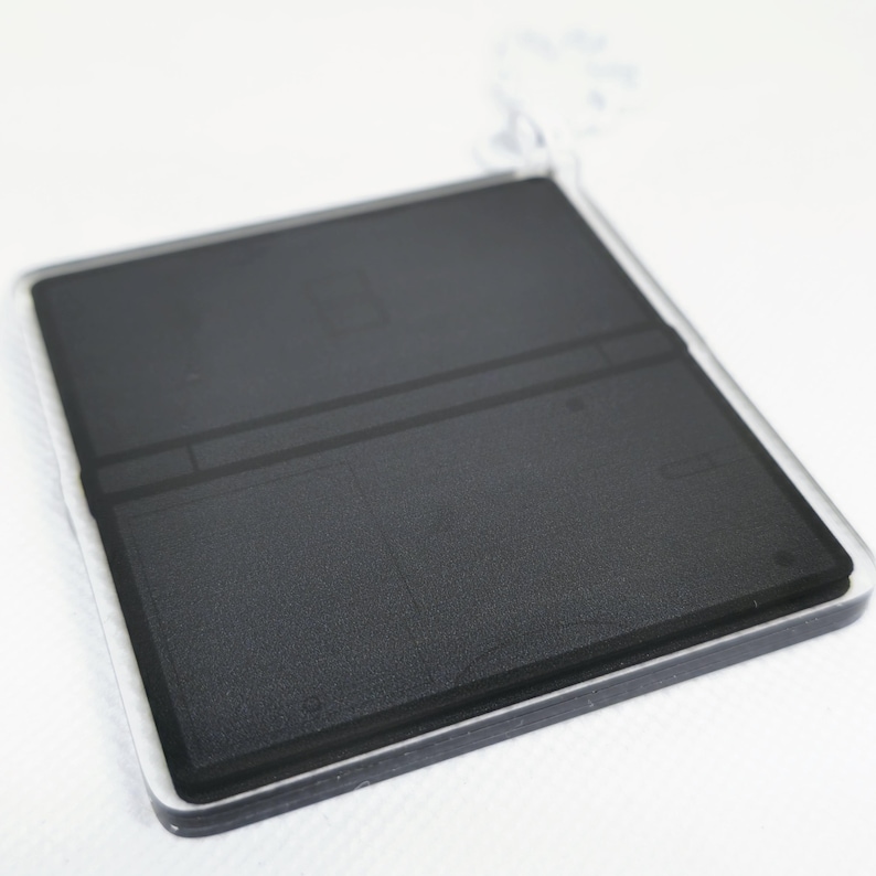 Op de afbeelding: Een zwart-witte sleutelhanger in de vorm van een draagbare gameconsole. De sleutelhanger is gemaakt van helder acryl en heeft een zwart-witte afbeelding van een gameconsole erop.