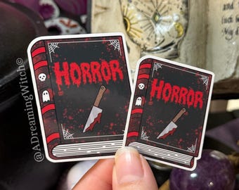 May include: Two rectangular stickers featuring a black book cover with the word HORROR in red dripping letters, a white knife with red blood stains, and small white spiderweb and ghost icons on the red spine and black cover edges.