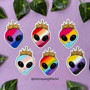 May include: Six alien head stickers, each wearing a gold crown with heart details. The aliens feature various color gradients including pink, purple, blue, orange, yellow, and rainbow patterns. The text ADreamingWitch is printed at the bottom center.