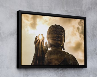 May include: A large bronze statue of Buddha with his hand raised, with the sun shining through his fingers. The statue is set against a cloudy sky.