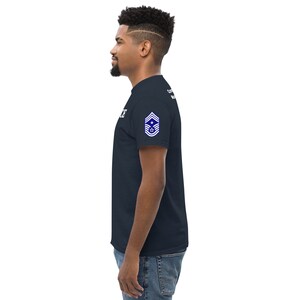 May include: A navy blue t-shirt with a white text design and a blue and white patch on the right sleeve. The patch features a star and stripes design.