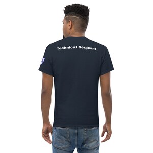 Peut inclure: T-shirt bleu marine avec l'inscription "Technical Sergeant" imprimée en blanc dans le haut du dos. La manche gauche présente un petit motif de drapeau américain. Le t-shirt est de style col rond classique.