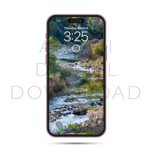 以下が含まれることがあります： ロック画面に、岩の多い風景を流れる川の写真が表示された紫色のiPhone。時間は3:25、日付は3月9日木曜日です。
