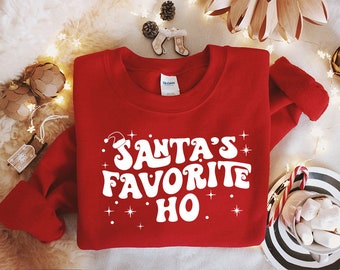 May include: Red Christmas sweatshirt with white text that reads "Santa's Favorite Ho!" with a small Santa hat graphic above the text.