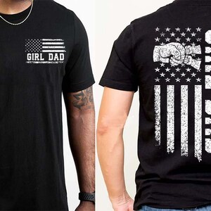 Puede incluir: Camiseta negra con un dise&ntilde;o de bandera americana desgastada. La parte delantera presenta la bandera y el texto "GIRL DAD". La parte trasera muestra un pu&ntilde;o dentro de la bandera y las palabras "GIRL DAD" verticalmente. Una camiseta informal para el uso diario.