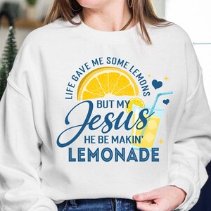 May include: White sweatshirt with a graphic design featuring a yellow lemon slice, a glass of lemonade, and the text "Life gave me some lemons but my Jesus he be makin' lemonade."