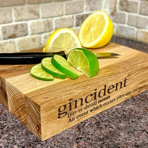 Op de afbeelding: Houten snijplank met het woord "gincident" en de definitie gegraveerd. Limoenen, citroenen en een mes met zwarte handgreep liggen op de plank. De plank is gemaakt van licht en donker hout.