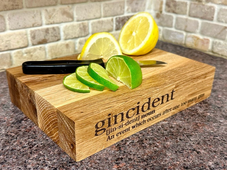 Op de afbeelding: Houten snijplank met het woord "gincident" en de definitie gegraveerd. Limoenen, citroenen en een mes met zwarte handgreep liggen op de plank. De plank is gemaakt van licht en donker hout.