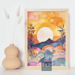 May include: A watercolour painting depicting a sunset over a landscape with hills and trees. The sun is a large, bright circle in the sky, and the hills are a mix of purple, blue, and green. The trees are silhouetted against the sunset. The painting is framed in a light wood frame. The text "IAP INKWELL ART PRINTS" is at the bottom of the painting.