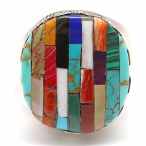 May include: A silver ring with a large oval inlay of colorful stones. The stones are arranged in a geometric pattern of rectangles and squares. The ring is a statement piece with a unique and eye-catching design.