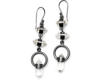 May include: A pair of silver earrings with clear crystal accents. The earrings feature a dangling crystal point, a hoop, and three crystal beads.