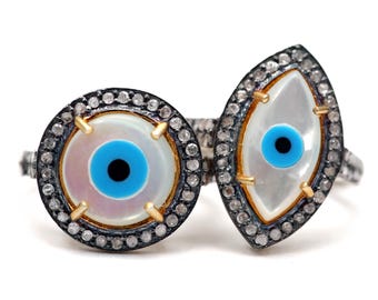 May include: A silver ring with two evil eye charms. The charms are made of mother of pearl with blue and black eyes. The ring is set with small diamonds.