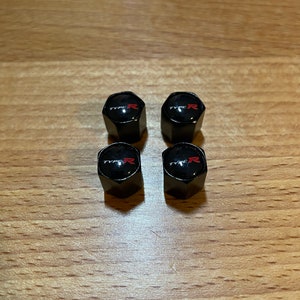 Peut inclure: Quatre capuchons de valve de pneu noirs avec un logo "TYPE R" rouge.