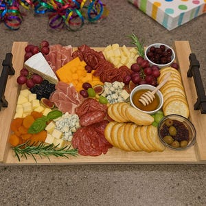 May include: A wooden charcuterie board filled with an assortment of cheeses, meats, crackers, grapes, and olives. The board includes a variety of cheeses, including brie, cheddar, and blue cheese. Garnished with rosemary and basil.