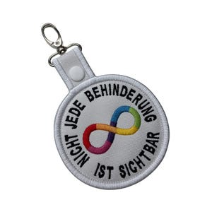 Könnte beinhalten: Ein weißer Schlüsselanhänger mit einem runden, gestickten Aufnäher. Der Aufnäher zeigt ein Regenbogen-Unendlichkeitszeichen und den Text "Nicht jede Behinderung ist sichtbar" in Schwarz. Ein silberfarbener Verschluss ist angebracht.