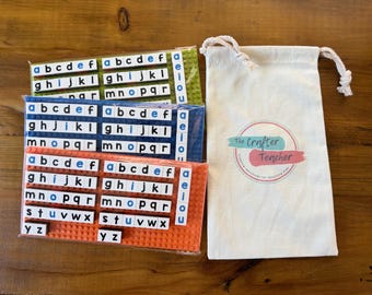 Puede incluir: Tres juegos de fichas de letras del alfabeto en una bolsa de plástico. Las fichas son de color verde, azul y naranja. Las fichas tienen letras blancas y contornos azules. La bolsa es blanca con el texto "The Crafter Teacher" impreso en ella.