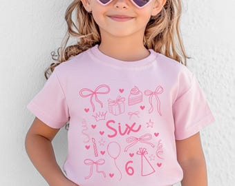 May include: Pink t-shirt with a pink graphic design of a birthday cake, presents, balloons, stars, hearts, and the word "Six".