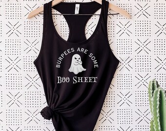 May include: Black racerback tank top with the text "Burpees are some Boo Sheet" and a ghost graphic. The shirt is hanging on a wooden hanger against a patterned white and black background. A cactus is visible on the right.