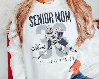 May include: White sweatshirt with the text "SENIOR MOM" above a hockey player graphic and the number "36". Below the graphic is the name "Noah" and the phrase "THE FINAL PERIOD". The word "WHITE" is in the bottom right corner.
