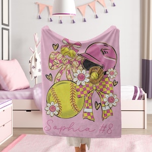 May include: Pink softball blanket with a softball, helmet, glove, and bows. The design includes the name "Sophia" and the number "8". The softball is yellow with red stitching, and the helmet is pink.