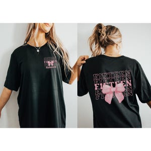 May include: Black t-shirt with a pink bow and the word "FIFTEEN" repeated multiple times on the back. The front of the shirt has the word "FIFTEEN" and the name "Mackenzie" printed on it.