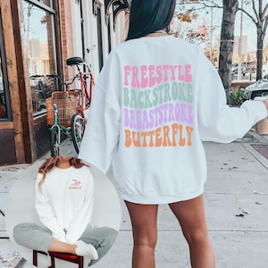 May include: White sweatshirt with the words "FREESTYLE", "BACKSTROKE", "BREASTSTROKE", and "BUTTERFLY" printed in a retro font in different colors. The words are stacked on top of each other.