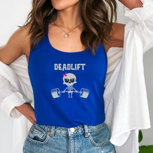 May include: A royal blue tank top with the word "DEADLIFT" above a skeleton lifting weights. The skeleton has a pink bow. The tank top is worn with blue jeans and a white shirt.