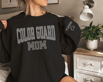 May include: Black sweatshirt with the text "Color Guard Mom" in white outlined letters. The left sleeve has the name "Marla" and a heart in white outlined letters.