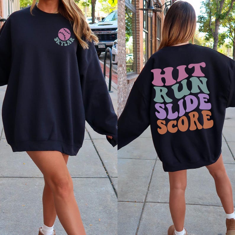 May include: Black sweatshirt with a baseball graphic and the name "Skylar" on the front. The back of the sweatshirt features the words "Hit Run Slide Score" in a colorful, retro font. A casual, sporty style.