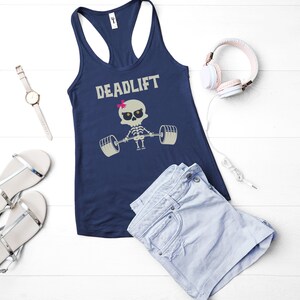 May include: Navy blue racerback tank top with the word "DEADLIFT" above a cartoon skeleton lifting weights. The skeleton has a pink bow. The image also includes a watch, sandals, shorts, and headphones.