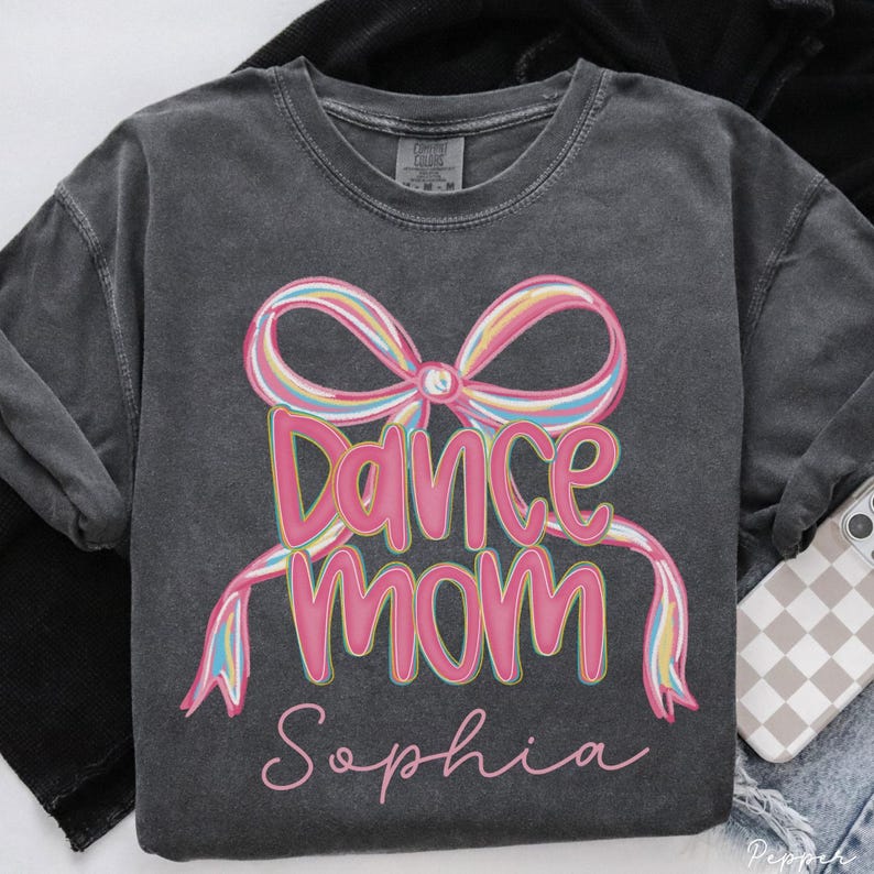 May include: Dark gray sweatshirt with the words "Dance Mom Sophia" in pink script, accented by a colorful bow graphic. The sweatshirt is a crew neck style and appears to be made of a soft material.
