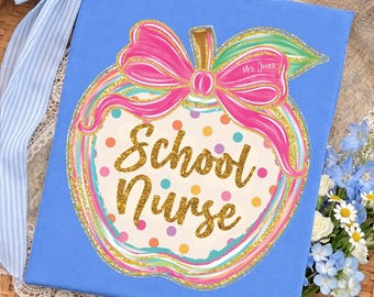May include: A square blue canvas featuring a central apple illustration with a pink bow, gold glitter accents, and multicolored polka dots. The text "School Nurse" is written in gold glitter script, with "Mrs. Jones" printed on the apple leaf.
