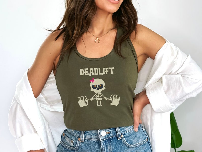 May include: Olive green tank top with the word "DEADLIFT" printed across the top. Below the text is a cartoon skeleton lifting weights. The skeleton has a pink bow on its head. The tank top is a racerback style.