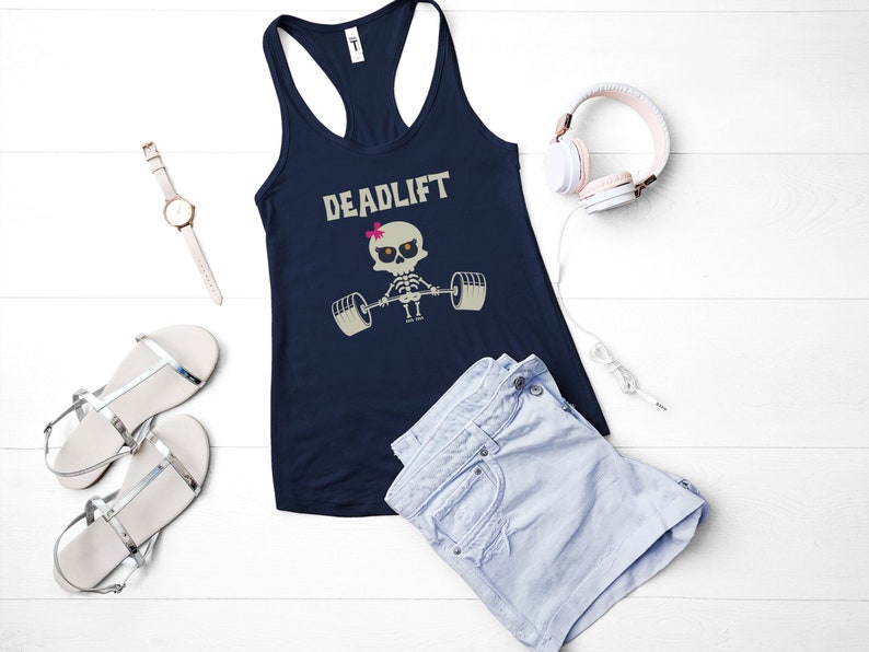May include: Navy blue tank top with the word "DEADLIFT" and a skeleton lifting weights graphic. The image also includes a pair of silver sandals, a watch, light blue shorts, and pink headphones.